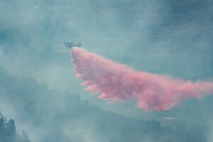 A plane releases red fire-retardant materials over a forest.
