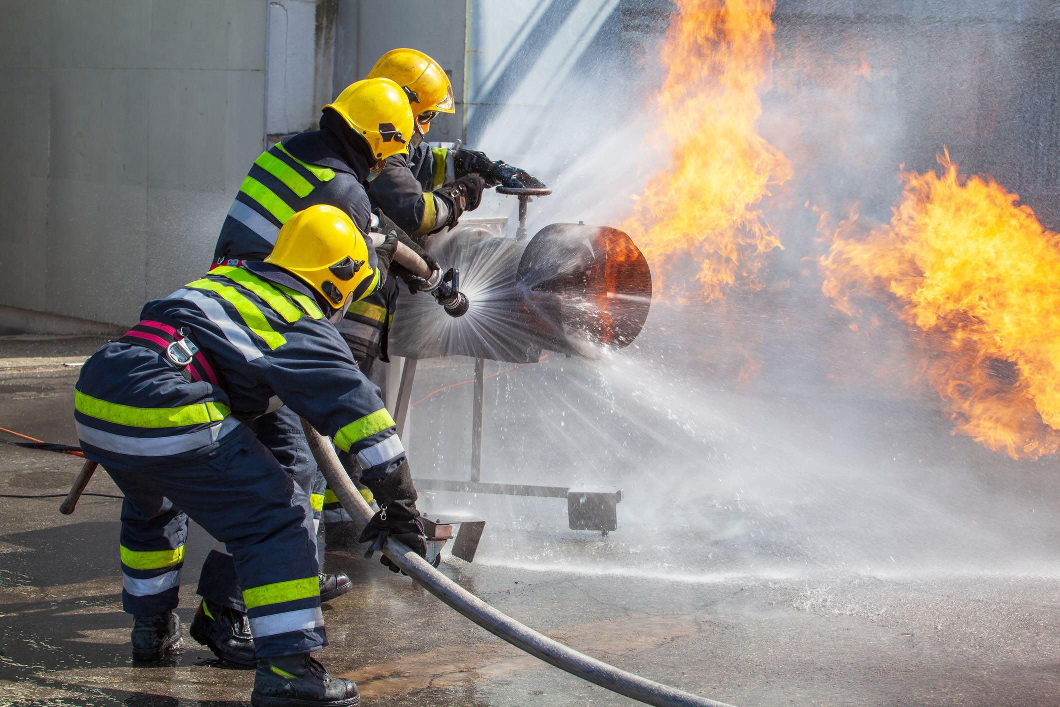 Three firefighters use water hoses to put out a fire in a training exercise.