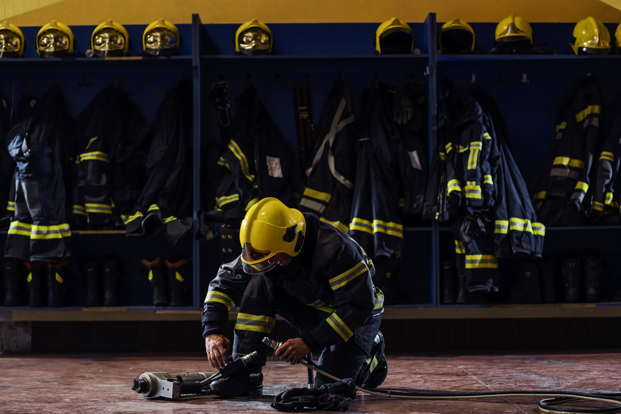 Fireman in protective uniform with helmet on head kneeling in fire station and preparing equipment for action.