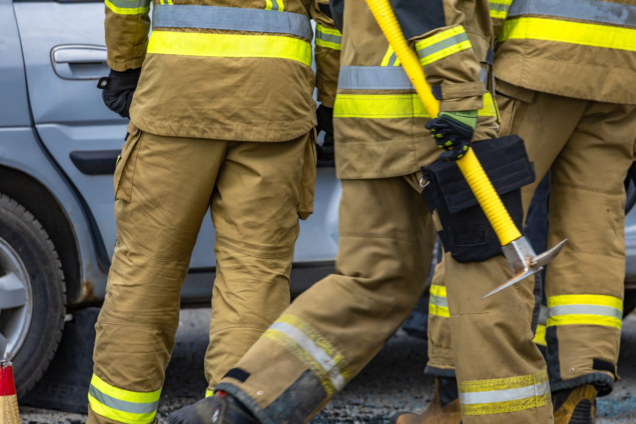 Firefighters wearing protective suits pulling a wounded man out of a car, a yellow pickaxe in the hands of a firefighter