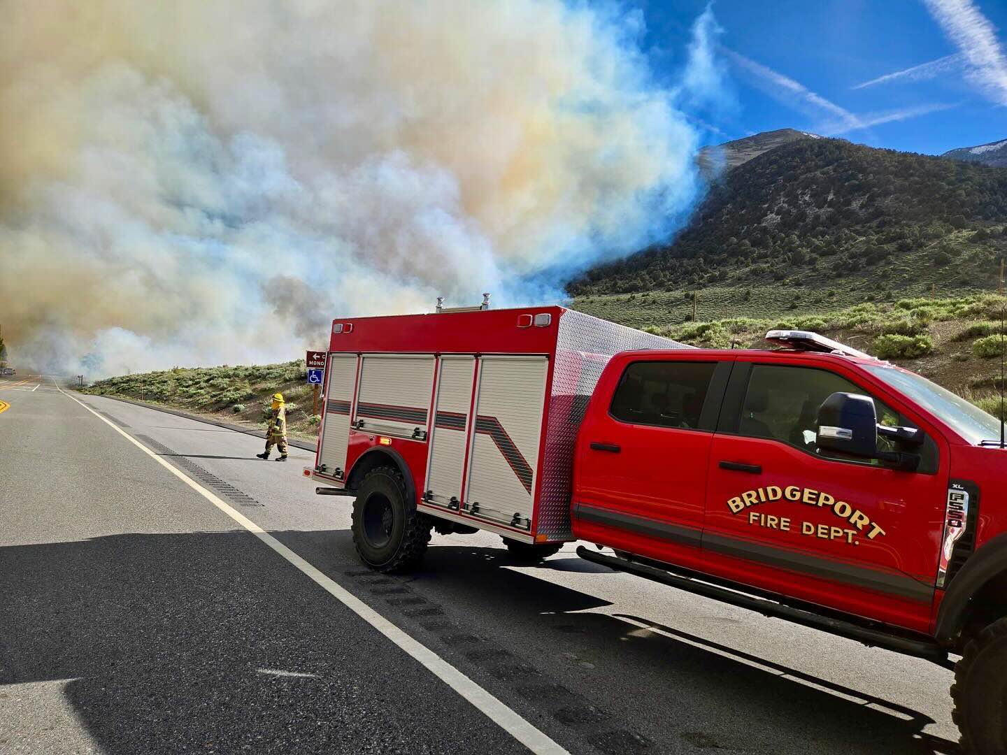 A fire truck from Bridgeport Fire Department is parked on a road next to a forest fire.